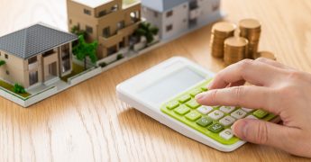 A hand tapping on a calculator with models of condos on the table